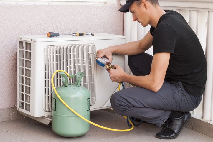 Técnico a inspecionar a unidade exterior de ar condicionado com garrafa de gás refrigerante